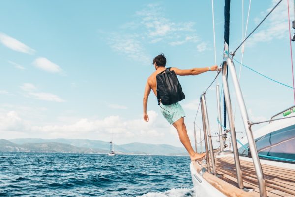 man-wearing-backpack-standing-on-side-of-boat-during-day